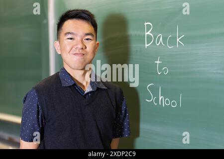 Un adolescent masculin souriant est debout devant un tableau noir avec les mots Back to School écrits sur moi Banque D'Images