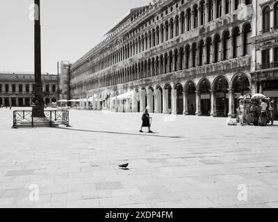 Venise, Italie - 30 juin 20220 photo en noir et blanc d'une femme âgée marchant à travers une piazza san marco vide avec un pigeon au premier plan Banque D'Images
