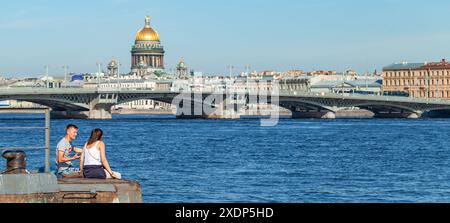 Saint-Pétersbourg, Russie - 28 juin 2018 : jeune couple assis à la jetée de la rivière Neva avec la cathédrale Isaakievsky sur le fond, photo panoramique Banque D'Images