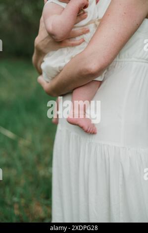 Mère tenant bébé en robe blanche, cadre extérieur. Banque D'Images