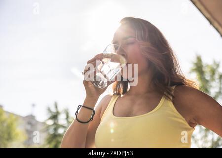 Une femme déshydratée boit de l'eau propre dans un verre pour reconstituer les liquides pendant les chaudes journées d'été. Banque D'Images