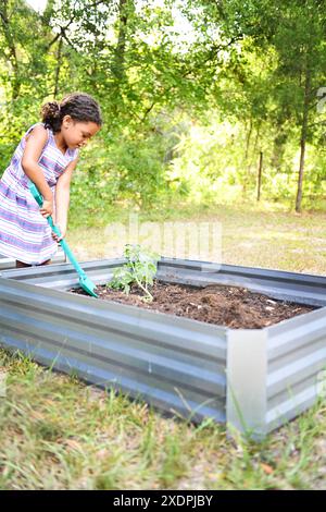 Fille creusant dans un lit de jardin, plantant un semis à l'extérieur. Banque D'Images