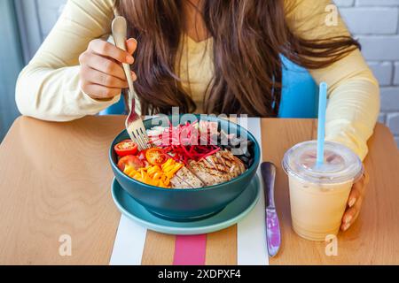 Jeune fille ayant une salade de quinoa avec des légumes frais servis dans un bol dans un restaurant de café sain et latte froid. Banque D'Images