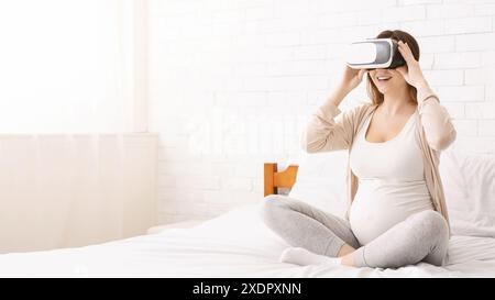 Femme enceinte utilisant le dispositif de réalité virtuelle sur le lit Banque D'Images