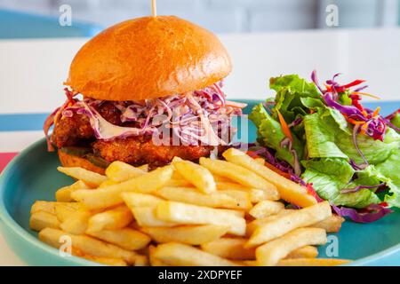 Hamburger de poulet frit glacé au miel dans un pain brioché servi avec des frites et une salade d'accompagnement sur une assiette dans un environnement de café. Banque D'Images