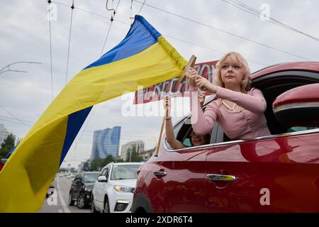 Petite fille ukrainienne agitant avec le drapeau national de l'Ukraine par une fenêtre de voiture pendant la manifestation pacifique à Kiev - 16 juin 2024 Banque D'Images