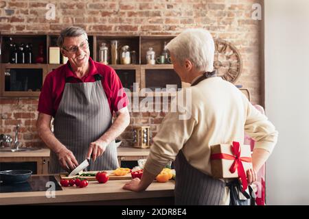 Couple senior aimant cuisiner ensemble dans la cuisine avec cadeau surprise Banque D'Images