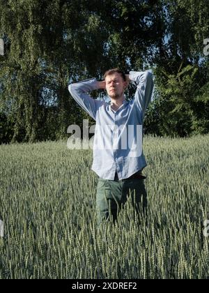 Portrait d'un jeune homme dans le champ vert ukrainien debout avec ses mains derrière la tête. Vue frontale verticale. Banque D'Images