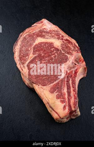 Côte de chianina vieillie crue et sèche de steak de bœuf offert en gros plan sur un tableau de design noir Banque D'Images