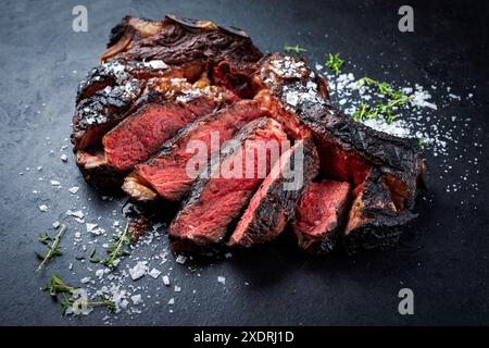 Côte de bœuf chianina séchée au barbecue servie avec du sel cristallin et du thym en gros plan sur un tableau noir Banque D'Images