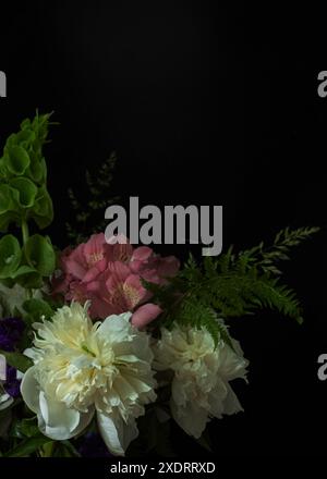 Élégant bouquet de fleurs mélangées comprenant des pivoines blanches, de l'alstroemeria rose et de la molucelle verte, disposées sur un fond noir. Photo basse fréquence Banque D'Images