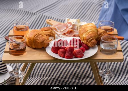 Une petite table servie avec de la nourriture pique-nique se dresse sur une clairière verte dans un parc de la ville. Fraises, croissants, fromage, collations, vin pique-nique en plein air, variou Banque D'Images