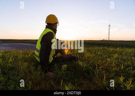 Le travailleur est assis sur l'herbe et regarde les éoliennes. Banque D'Images