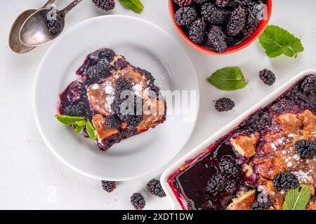 Tarte de cordonnier de mûrier maison sucrée, gâteau de cordonnier de baies d'été doux dans un plat de cuisson en émail et une assiette, sur un espace de copie de table de cuisine blanc Banque D'Images