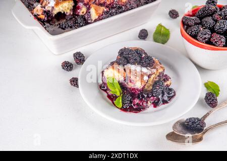 Tarte de cordonnier de mûrier maison sucrée, gâteau de cordonnier de baies d'été doux dans un plat de cuisson en émail et une assiette, sur un espace de copie de table de cuisine blanc Banque D'Images