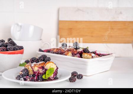 Tarte de cordonnier de mûrier maison sucrée, gâteau de cordonnier de baies d'été doux dans un plat de cuisson en émail et une assiette, sur un espace de copie de table de cuisine blanc Banque D'Images