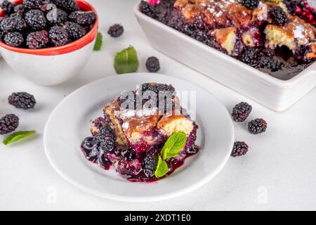 Tarte de cordonnier de mûrier maison sucrée, gâteau de cordonnier de baies d'été doux dans un plat de cuisson en émail et une assiette, sur un espace de copie de table de cuisine blanc Banque D'Images