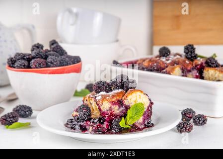 Tarte de cordonnier de mûrier maison sucrée, gâteau de cordonnier de baies d'été doux dans un plat de cuisson en émail et une assiette, sur un espace de copie de table de cuisine blanc Banque D'Images