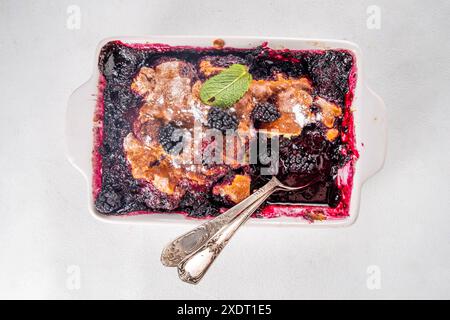 Tarte de cordonnier de mûrier maison sucrée, gâteau de cordonnier de baies d'été doux dans un plat de cuisson en émail et une assiette, sur un espace de copie de table de cuisine blanc Banque D'Images