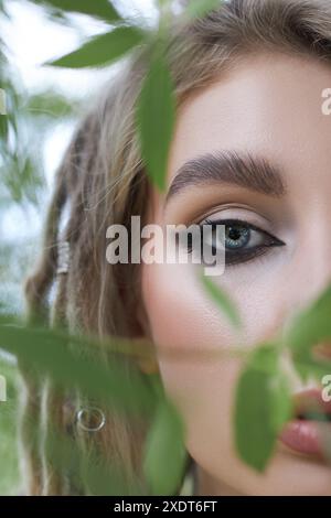 Gros plan d'un œil de femme jetant un coup d'œil à travers le feuillage vert, l'image capture un sentiment de mystère et d'intrigue. Banque D'Images