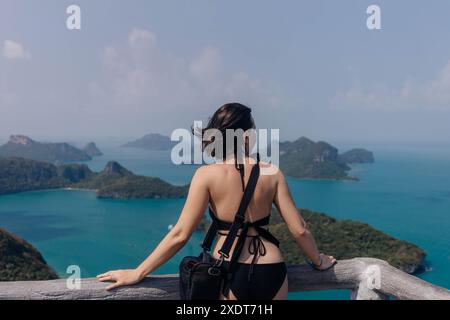 Une femme en maillot de bain noir se tient sur une plate-forme d'observation, regardant la vue imprenable sur une chaîne d'îles en Thaïlande. Banque D'Images