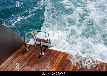 Pont arrière en bois de teck et échelle métallique d'un yacht à moteur, vagues et éclaboussures de mer et mousse. Banque D'Images