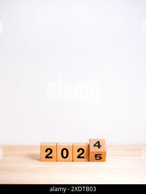 2025 bonne année avec changement aux concepts de la nouvelle ère. Retournement des numéros de calendrier de 2024 à 2025 ans sur des blocs de cube en bois isolés sur une table en bois et whit Banque D'Images