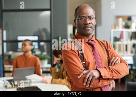 Portrait vers le haut de la taille d'un homme senior noir confiant posant dans le bureau debout avec les bras croisés et regardant l'appareil photo avec l'espace de copie d'expression sérieuse Banque D'Images
