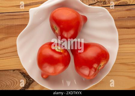 Plusieurs tomates juteuses rouges avec plaque en céramique blanche sur table en bois, macro, vue de dessus. Banque D'Images