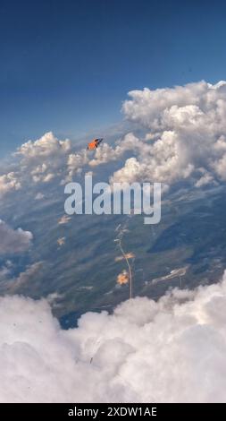 Vue aérienne d'une personne en wingsuit volant au-dessus des nuages avec un ciel dégagé et un paysage en dessous. Banque D'Images