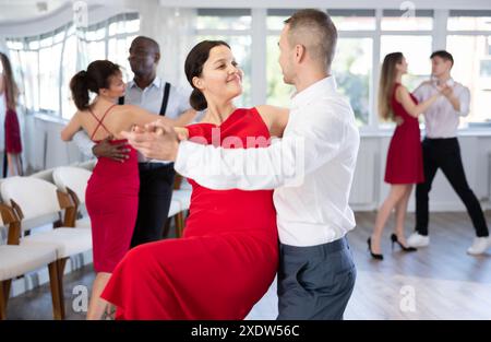 Jeune femme souriante en robe rouge et partenaire accomplissent avec succès des mouvements fascinants de la danse paso doble pendant la fête de danse Banque D'Images