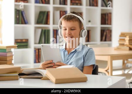 Adolescent dans des écouteurs avec tablette à la bibliothèque Banque D'Images