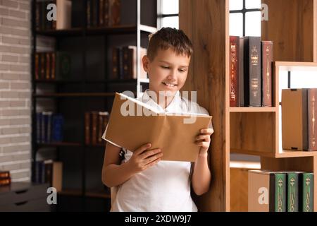 Adolescent lisant le livre près de l'étagère dans la bibliothèque Banque D'Images