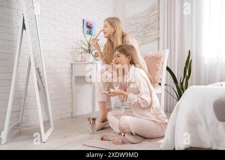 Belles jeunes sœurs heureuses en pyjama se maquillant à la maison Banque D'Images