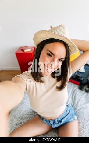 Jeune femme prenant le selfie tout en préparant la valise de vacances d'été à la maison Banque D'Images