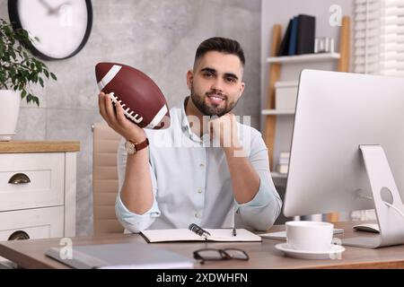 Jeune homme avec ballon de football américain à table dans le bureau Banque D'Images