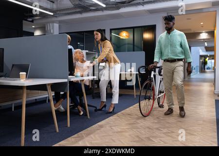 Discuter du travail, groupe diversifié de collègues d'affaires avec l'homme marchant vélo dans le bureau Banque D'Images