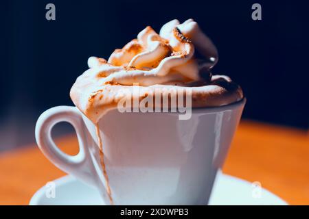 Tasse à café avec crème fouettée sur le dessus. Délicieuse et crémeuse friandise matinale. La tasse est placée sur une table en bois dans le café Banque D'Images