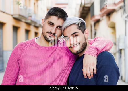 Couple gay souriant à la caméra dans la rue de la ville. Les amoureux masculins s'embrassent. Concept de style de vie LGBT Banque D'Images