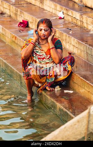 Inde, Uttar Pradesh, Varanasi. Une femme dans un sari coloré sur les marches d'un ghat se lave dans le Gange. Banque D'Images