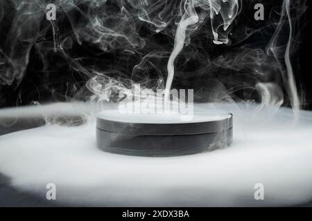 Conteneur rond noir émet une fumée blanche dense, créant une atmosphère mystérieuse et intrigante. La fumée tourbillonne et monte, ajoutant à th Banque D'Images