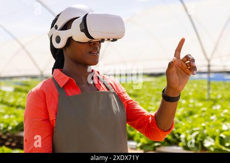 En utilisant un casque VR, agricultrice gérant une ferme maraîchère hydroponique en serre Banque D'Images