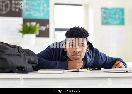 À l'école, un adolescent afro-américain reposant la tête sur le bureau, regardant réfléchi Banque D'Images