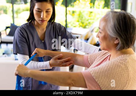 Infirmière asiatique aidant une femme âgée à faire des exercices de résistance à domicile Banque D'Images