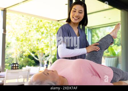 Physiothérapeute féminine aidant une femme âgée avec des exercices de jambe à la maison Banque D'Images