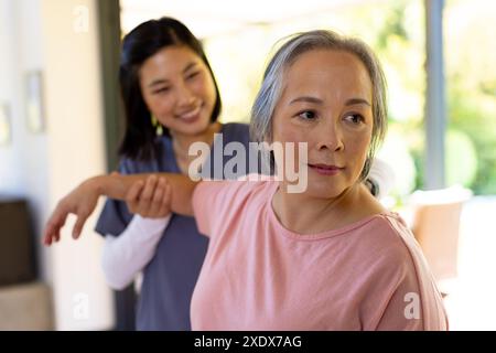 Physiothérapeute féminin asiatique aidant la femme âgée avec l'exercice du bras à la maison Banque D'Images