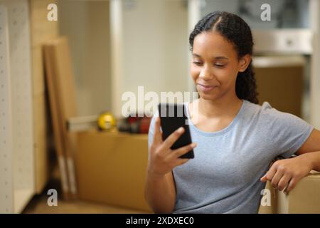 Femme noire vérifiant le téléphone intelligent rénover la maison Banque D'Images