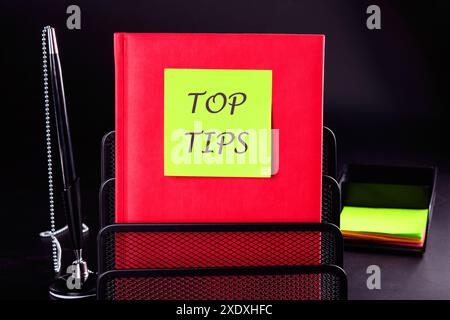 Texte TOP TIPS concept d'entreprise. CONSEILS SUPÉRIEURS sur un autocollant sur un carnet rouge sur un fond noir Banque D'Images