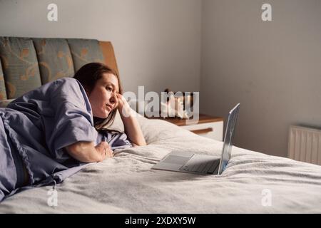 Une femme est confortablement allongée sur son lit, immergée dans le monde numérique grâce à son ordinateur portable Banque D'Images