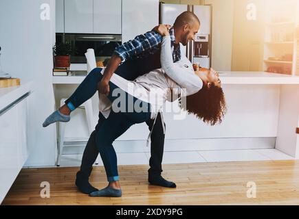 Danse, romance et sourire avec couple dans la cuisine de la maison ensemble pour le lien, l'amour ou la musique. Énergie, heureux ou relation avec l'homme et la femme en mouvement Banque D'Images